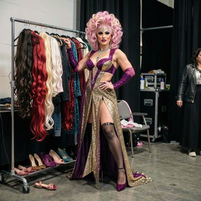 a drag performer's costume rail backstage with wigs and heels