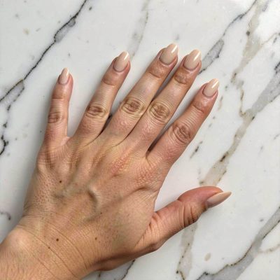 a hand with nude nails against a marble surface